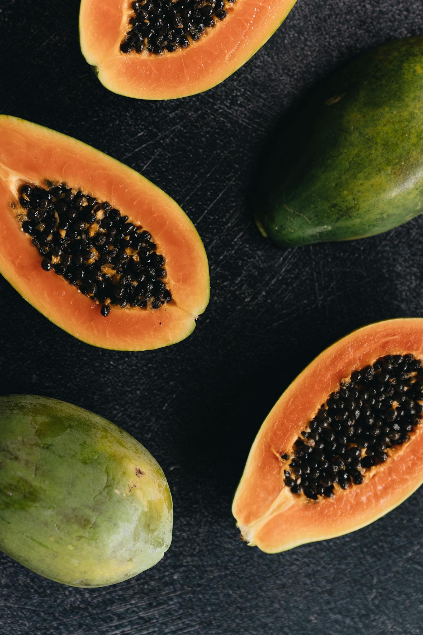 Top view of delicious ripe papaya halves and whole papaya placed on black wooden surface illustrating natural organic healthy food concept